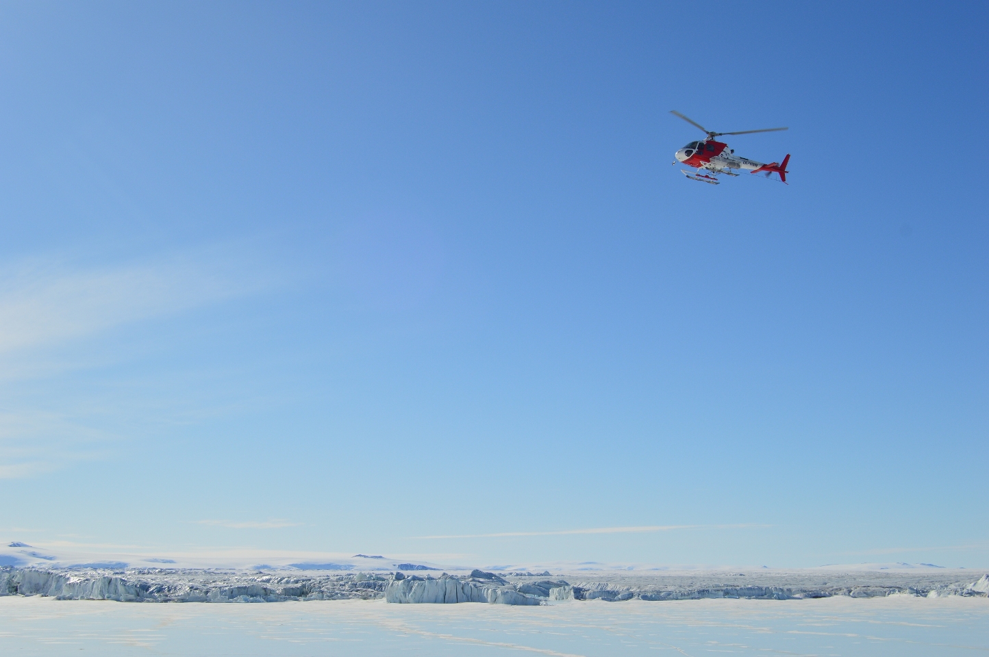 helicopter flying in blue sky over ice