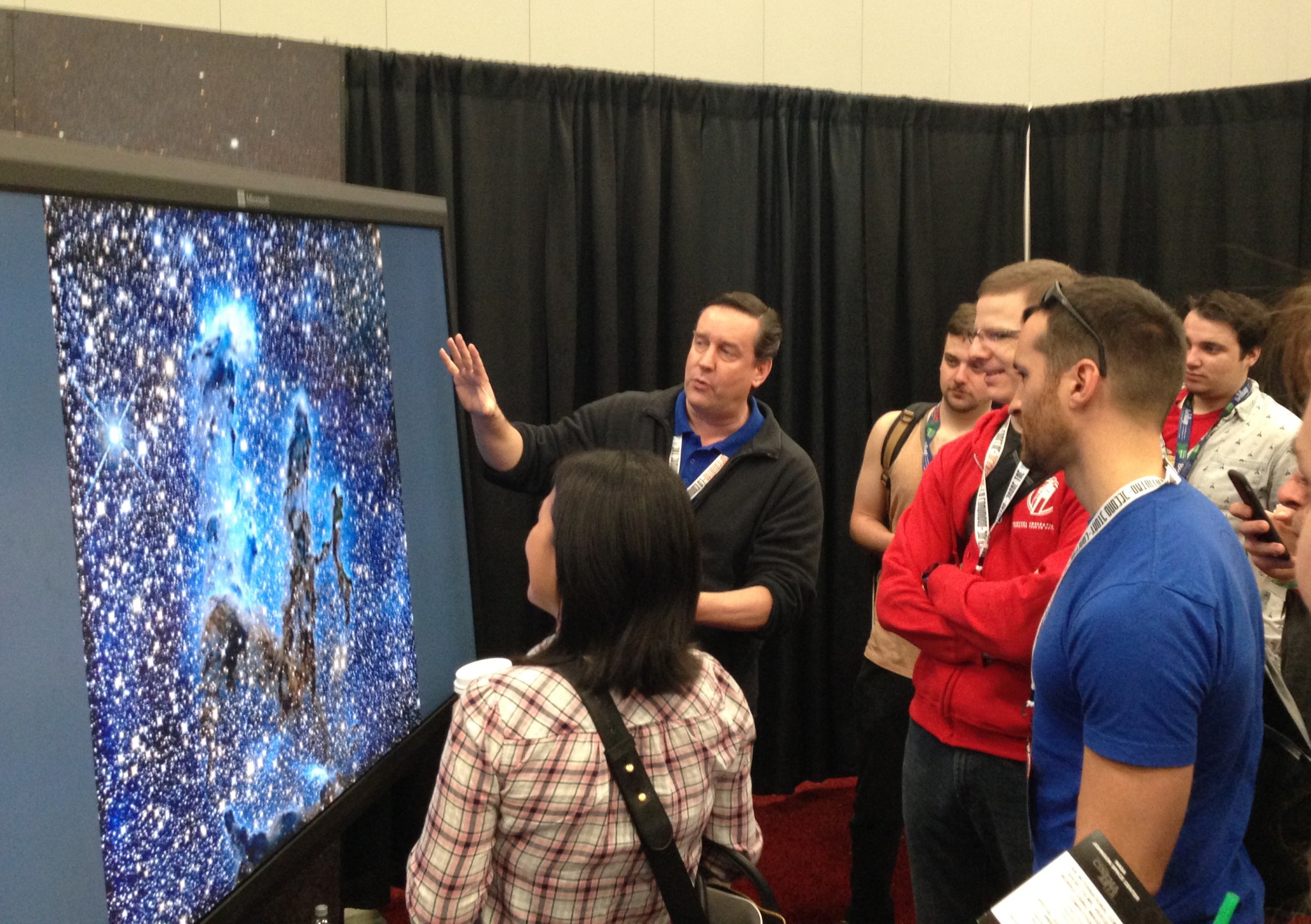Visitors listen to an explanation of how the Webb telescope will see the famous Eagle Nebula in infrared light at the NASA Booth