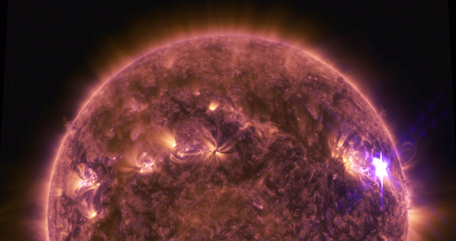 An image of the Sun during a solar flare. The Sun appears as a half circle filling most of the image, its surface appearing in purple and orange swirls with darker and lighter areas. The solar flare appears as a bright, whitish-purple spot on the right side of the Sun, with faint, light orange filaments looping out of it and brighter orange glow shining out of that area. The background is solid black.