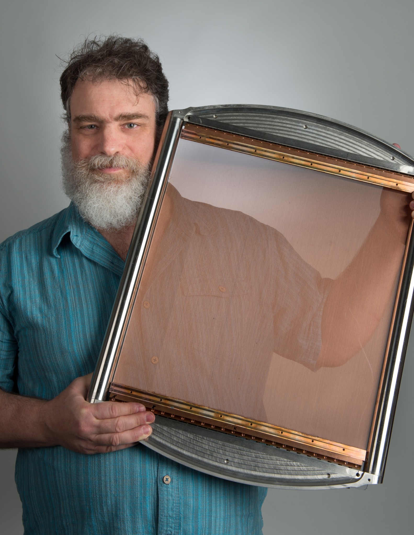 Paul Mirel standing with a metal frame filled with very thin copper filaments making a grid.