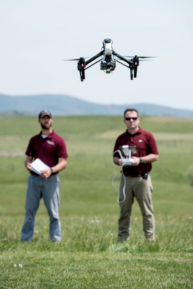 Two men flying a drone that is hovering just over their heads