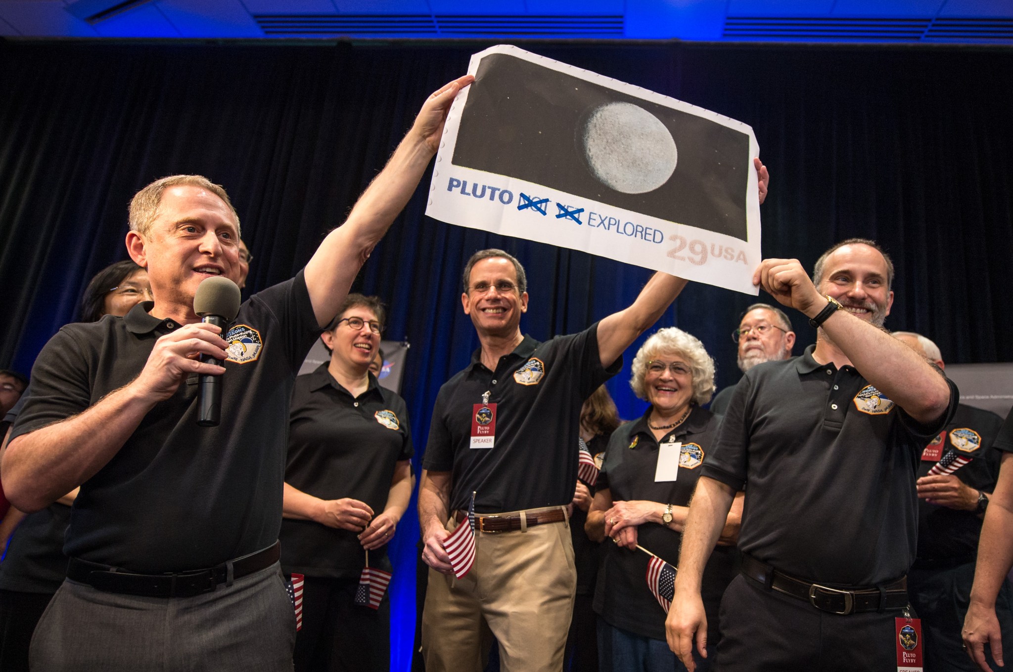 New Horizons Principal Investigator hold a print of the 1991 Pluto stamp (with their suggested update) on July 14 at APL