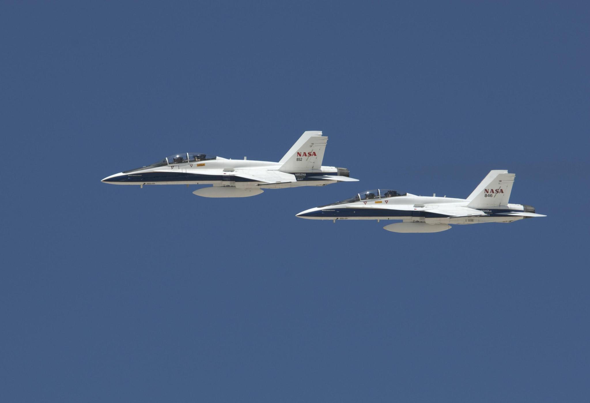 Two F/A-18B aircraft in flight in formation against blue skies.