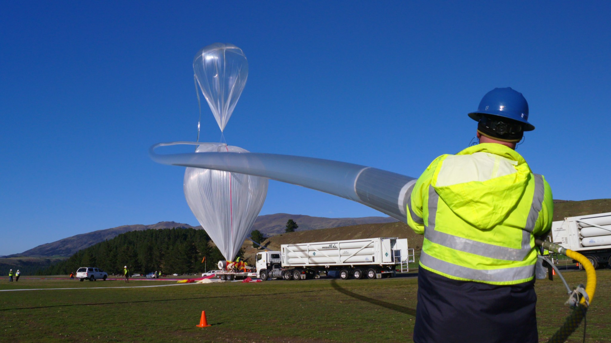 A technician holds a long tube that leads to a super pressure balloon being inflated in the background.