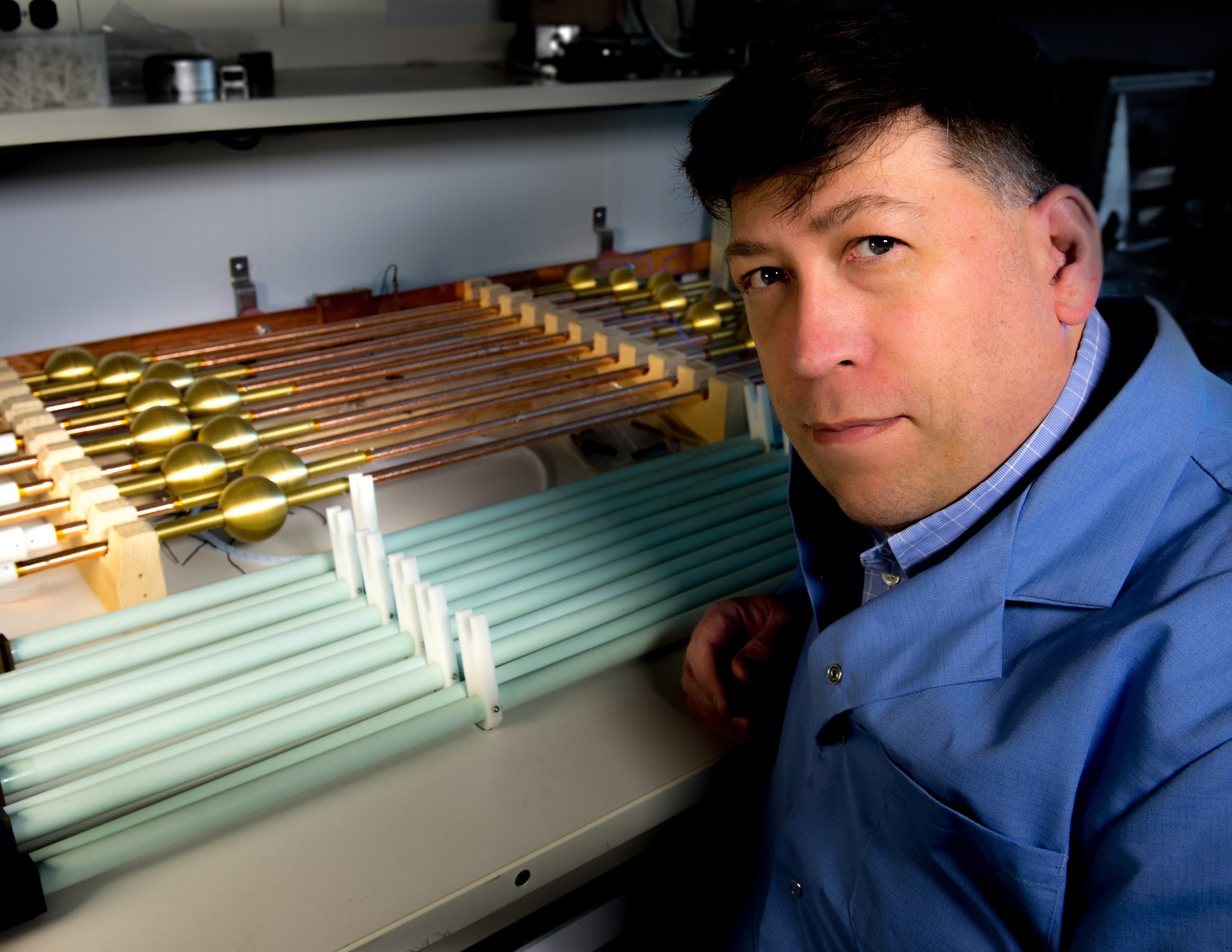 Doug Rowland kneels in front of a row of copper pipes, each with a gold ball on it.