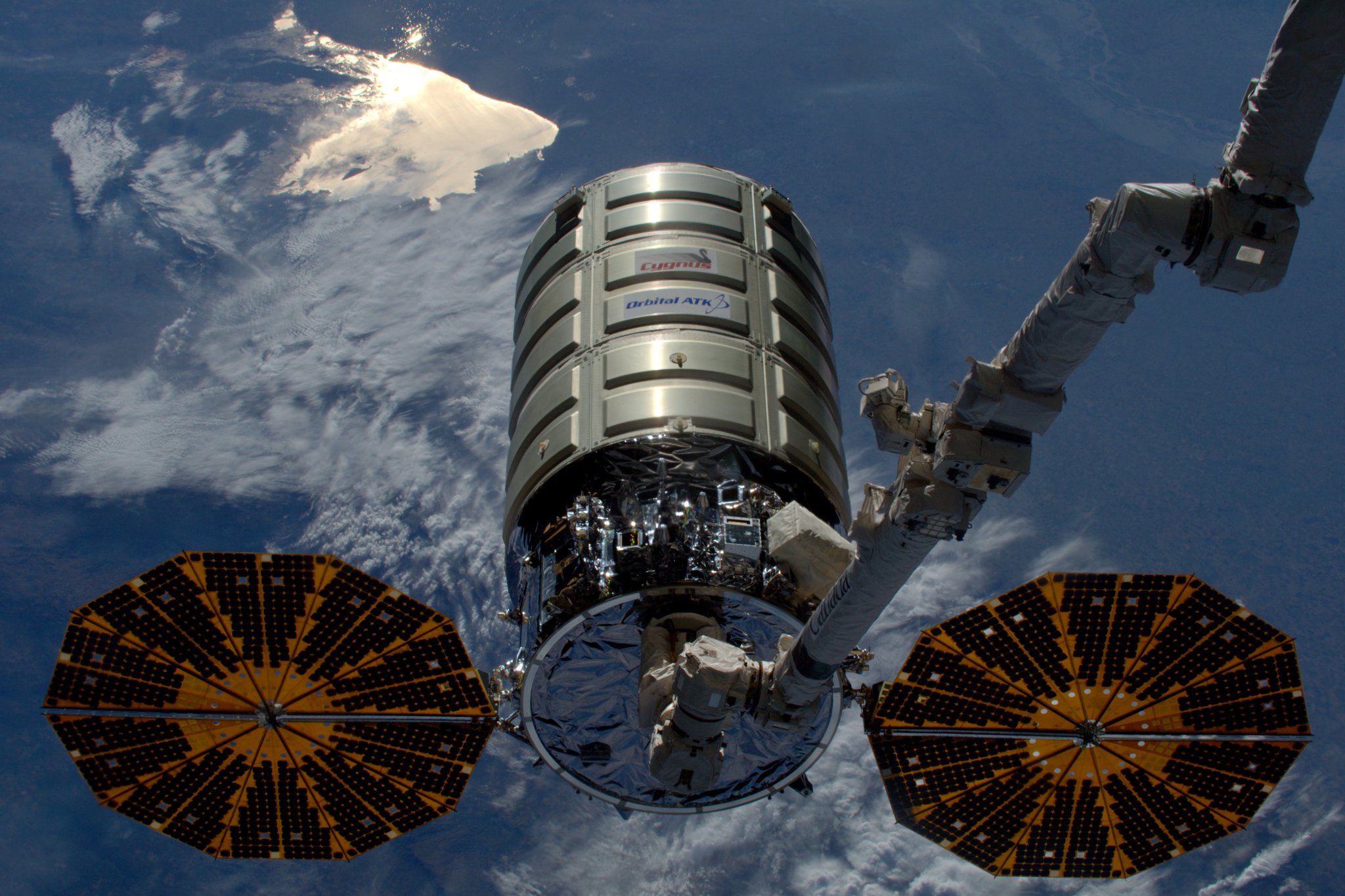 Cygnus spacecraft and robotic arm of space station closeup with Earth visible below