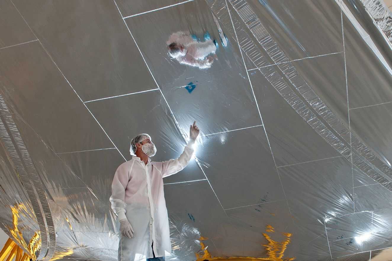 An engineer in a cleanroom looks at one of the sunshield layers that shows a grid pattern of "rip-stops."