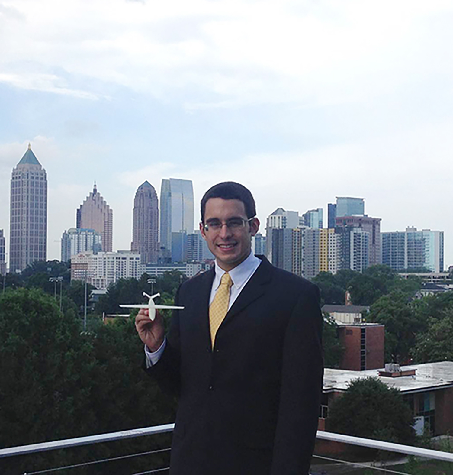 Man in a suit with a city in the background holding a model plane.