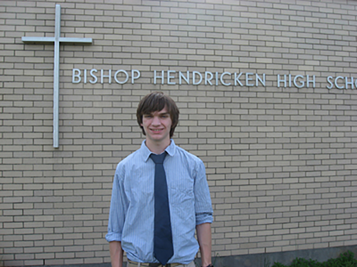 2nd place winner, male student standing in front of his school.