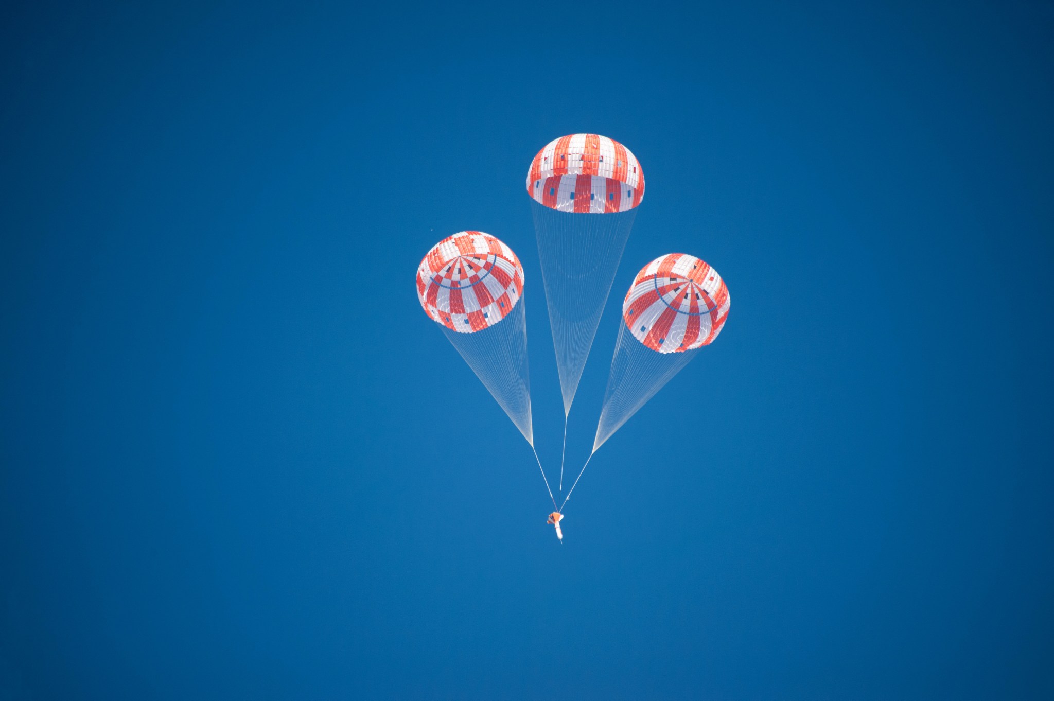An Orion test article descends under three main parachutes