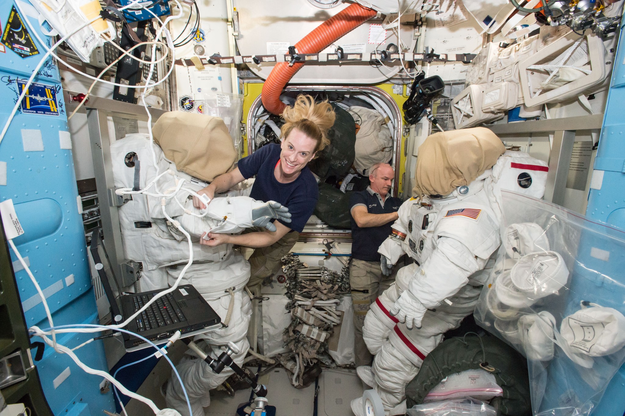 Astronauts Kate Rubins and Jeff Williams inside airlock, examining spacesuits