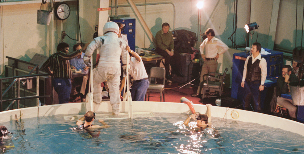 A person in a space suit steps out of the water immersion facility at JSC