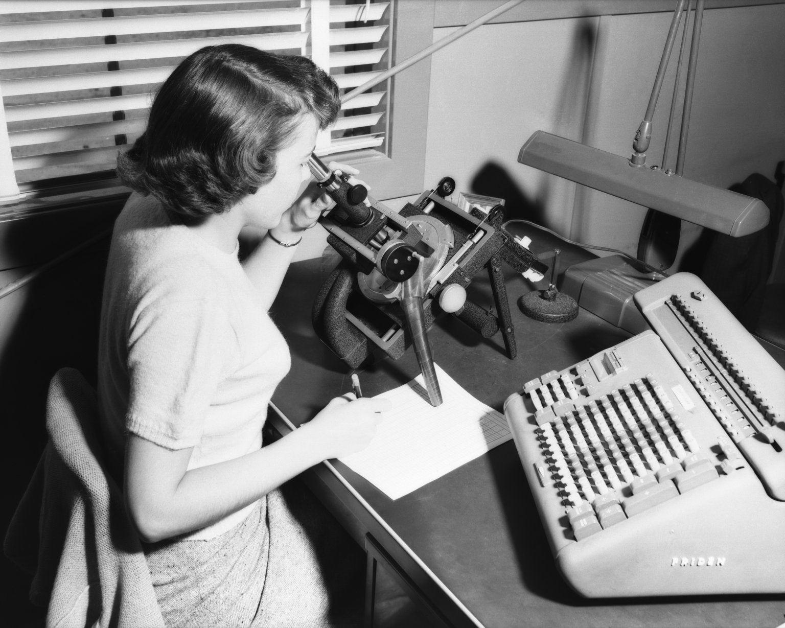 Computer at her work with microscope and the Friden calculating machine.
