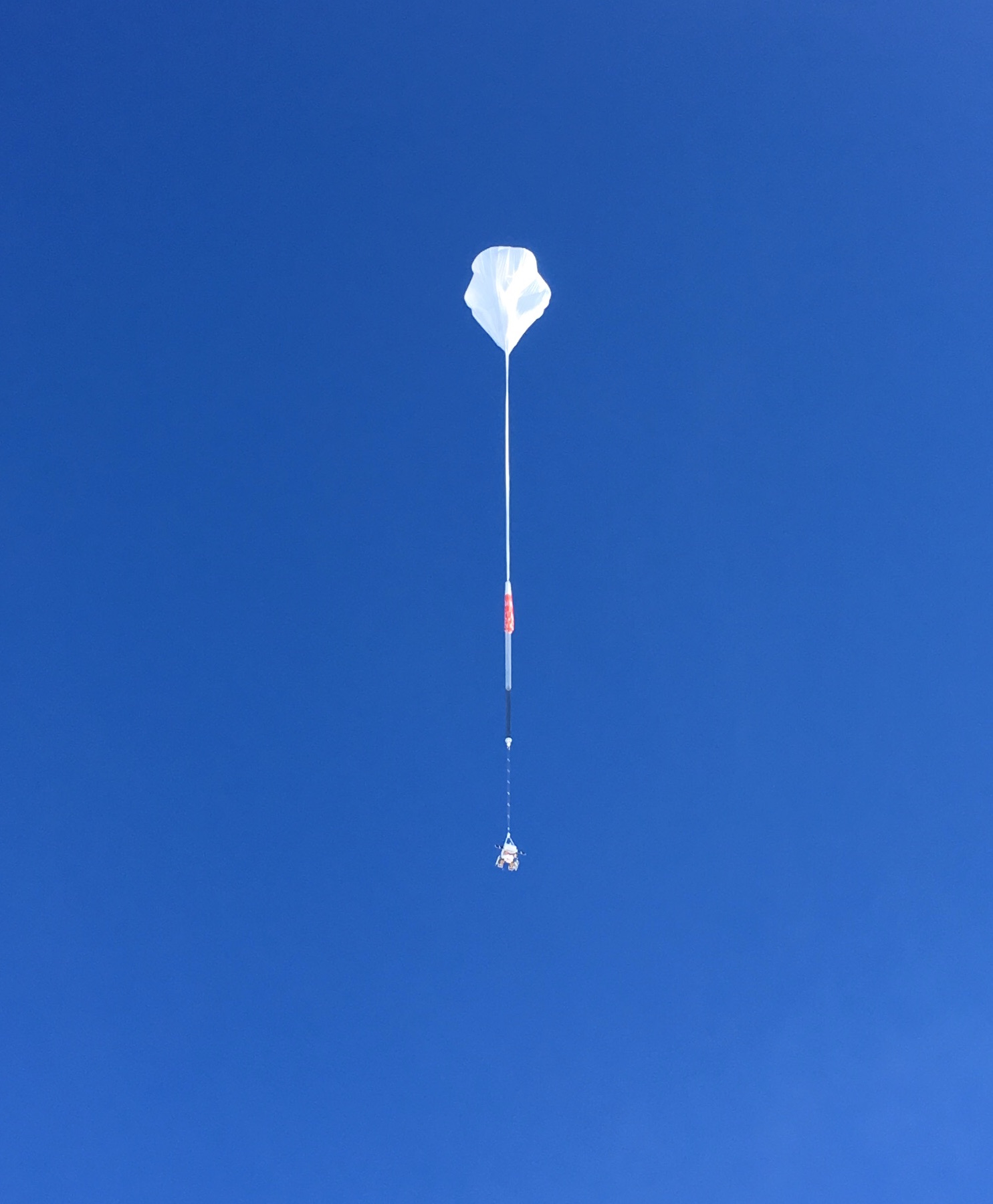 A scientific balloon after take off in the sky, partially inflated.