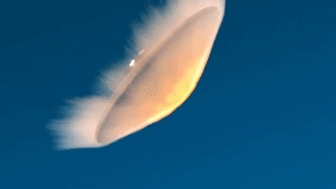 A space vehicle enters an blue-sky atmosphere with the underside of its conical aeroshell glowing with heat