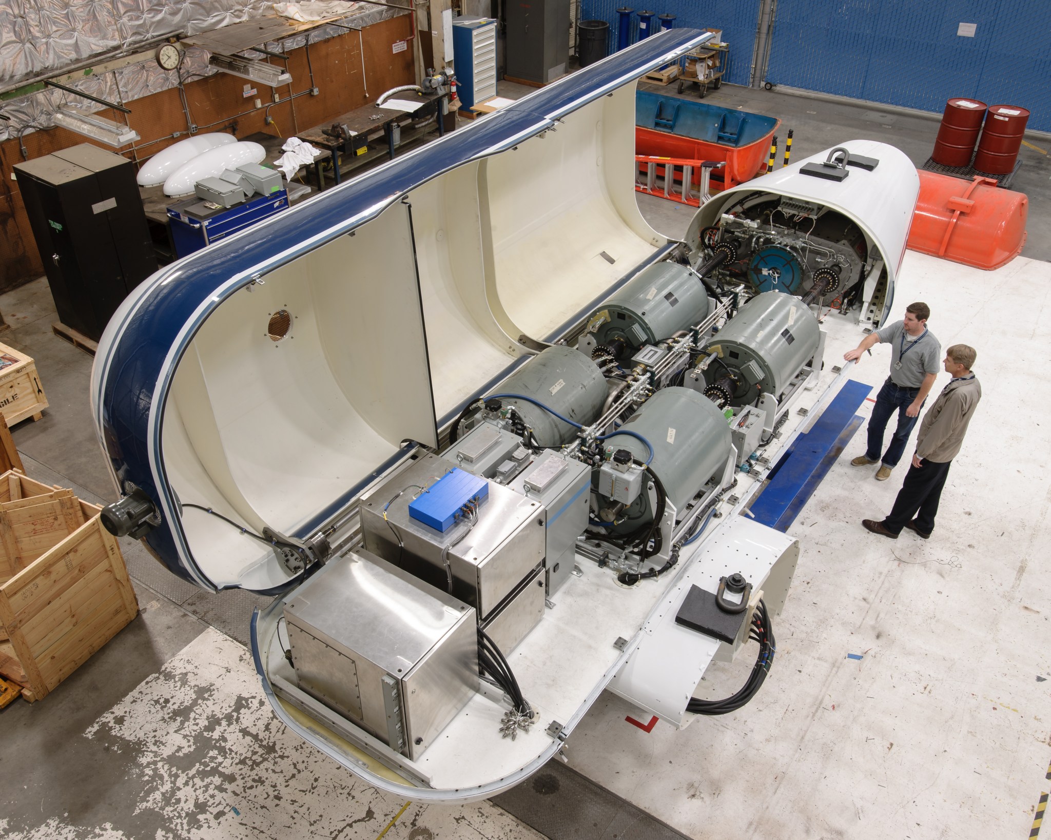 The Tiltrotor Test Rig aerodynamic shell is open while two employees are looking inside.