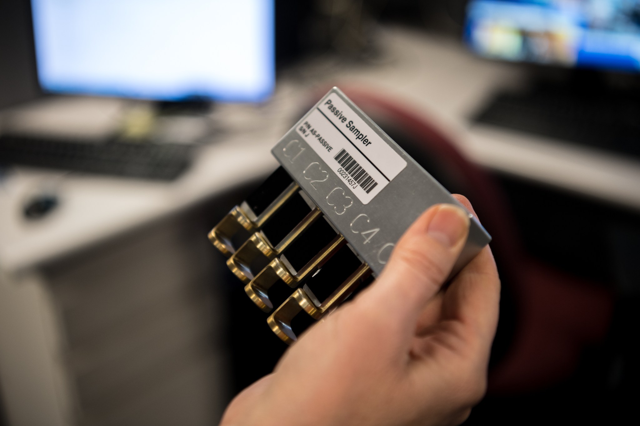 A hand is holding the passive air sampler that has several plates with sticky surfaces that collect large particulates floating inside the space station.