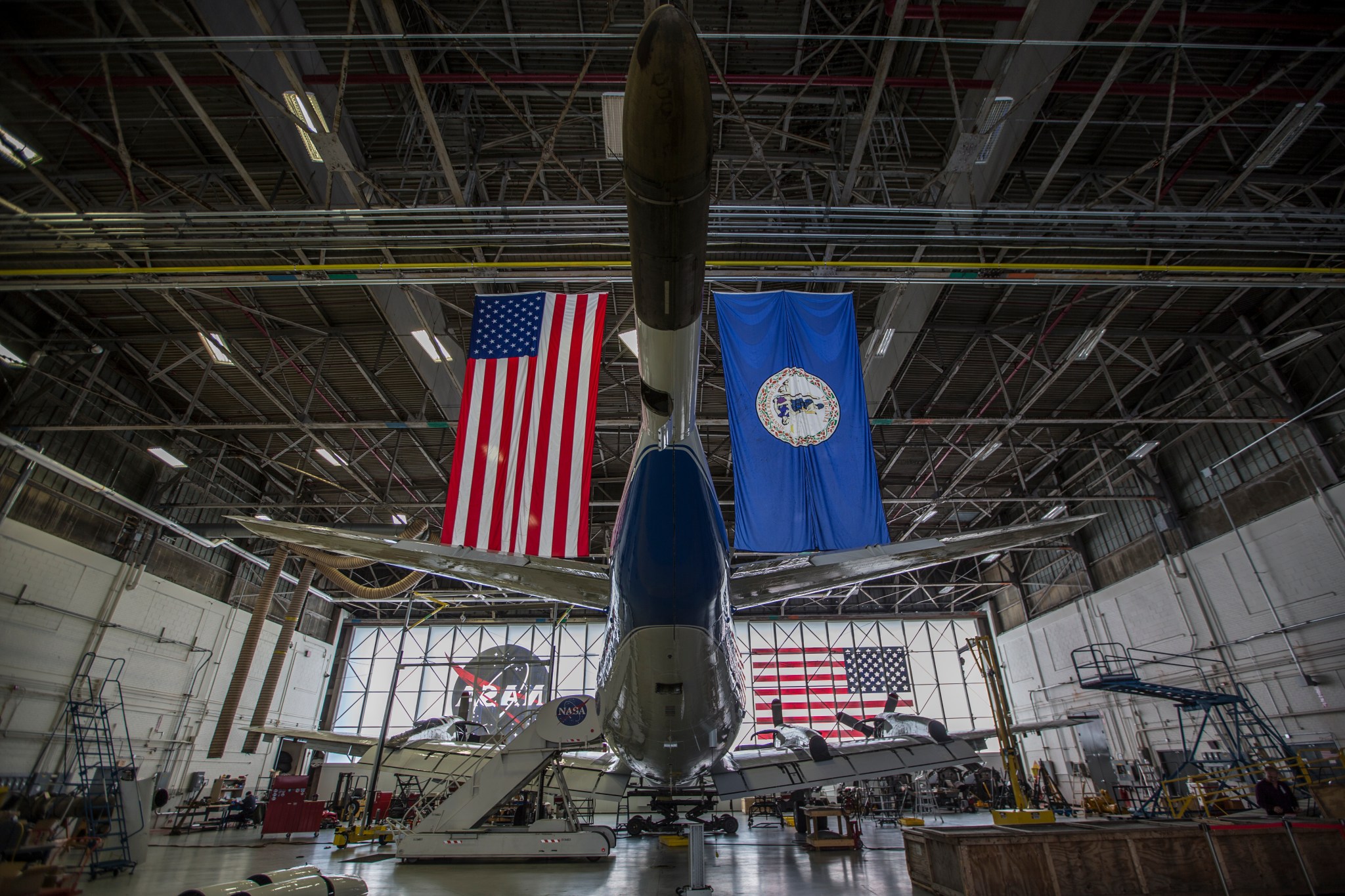 The back end of the P-3 aircraft inside of a plane hangar. Above the plane hangs an American Flag and Virginia state flag.