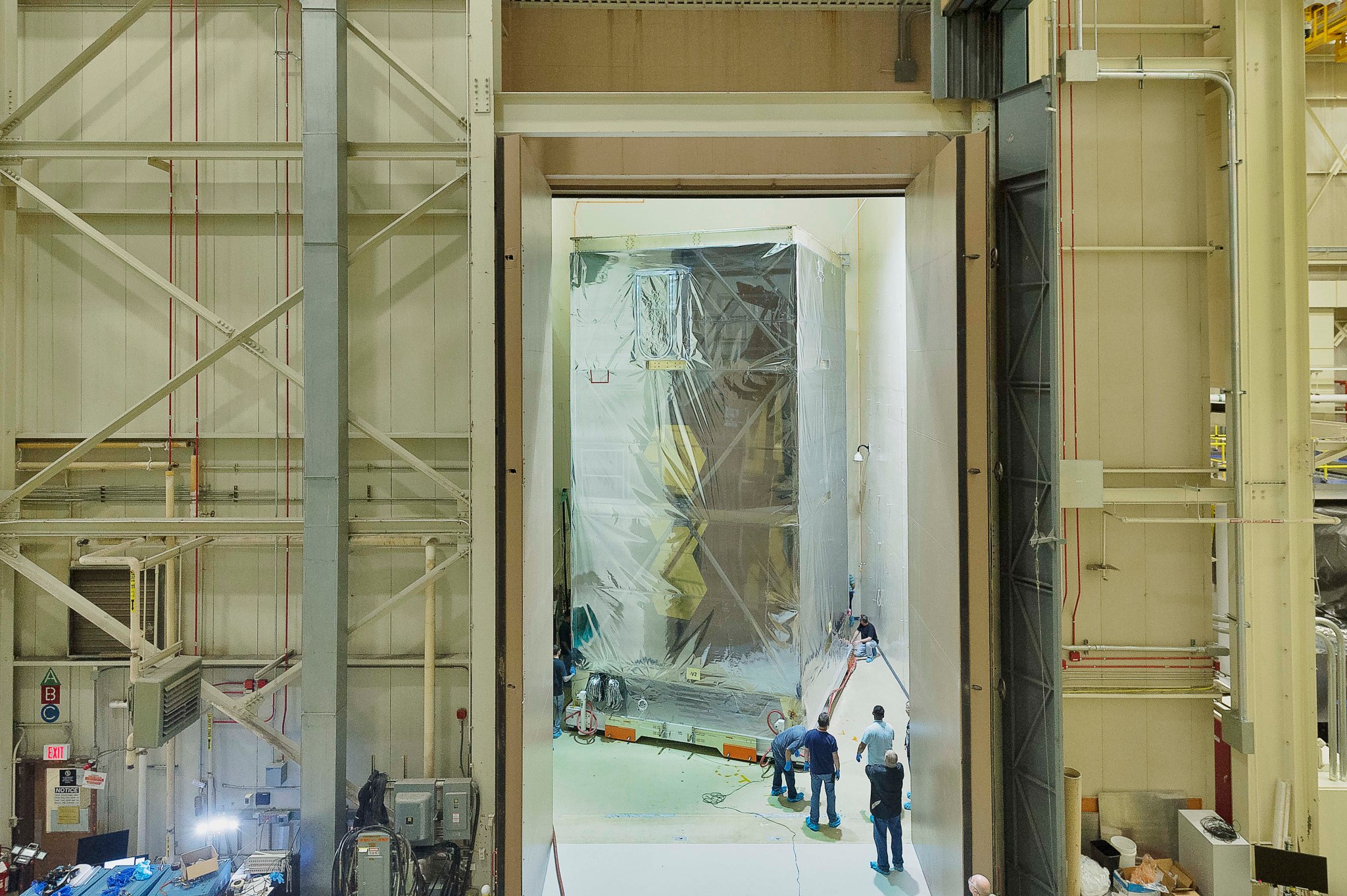 A huge partially transparent box is moved into the acoustic chamber, which a small but very tall room. Doors that are several inches thick are open, showing the room and the box. Through the box walls, you can just see gold hexagon mirrors.