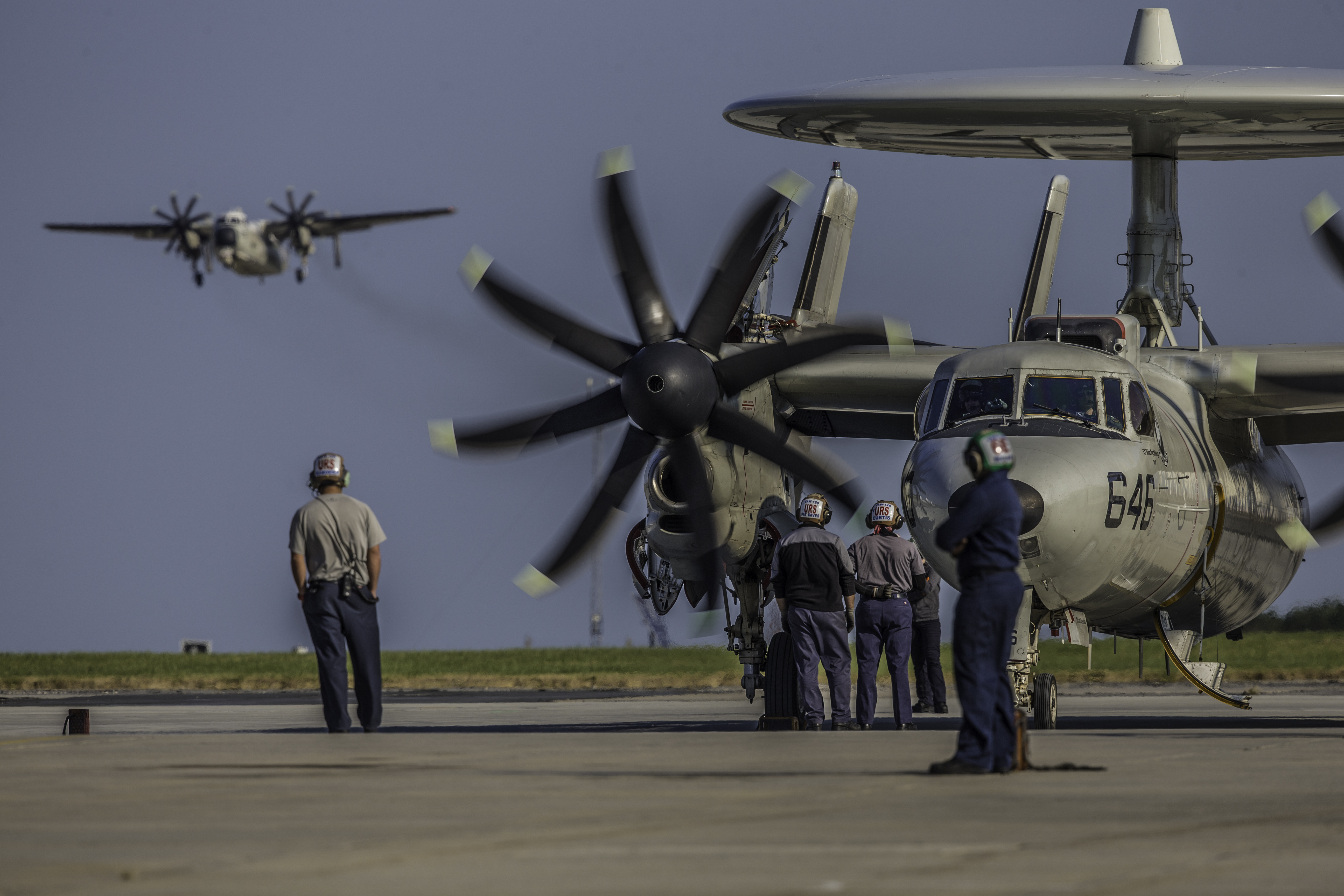 Technicians stand around an E-2 Navy aircraft.