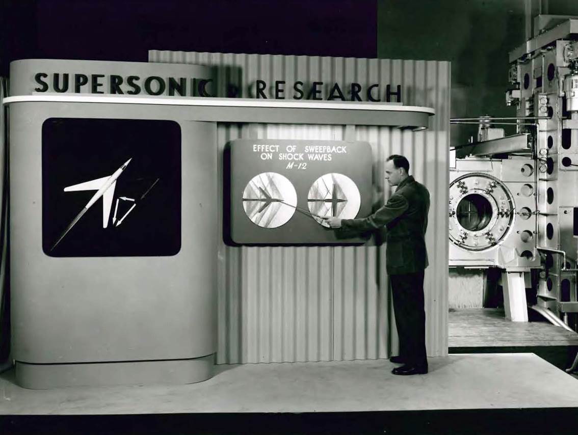 Walter Vincenti explaining the benefits of wing sweep, in front of the test section of the 1-by-3-foot supersonic wind tunnel.