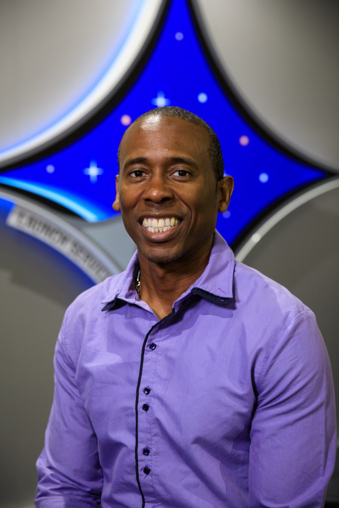 A portrait of Kennedy Space Center's Denton Gibson with the Launch Services Program insignia in the background.