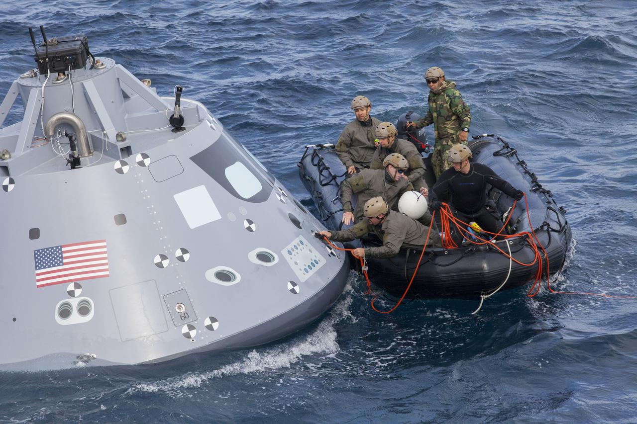 Navy divers in a small zodiac boat attaching red rope to Orion spacecraft in ocean