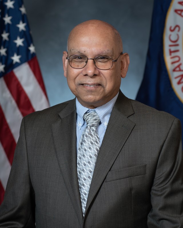 Portrait of Ajay Misra with U.S. and NASA flags in background.