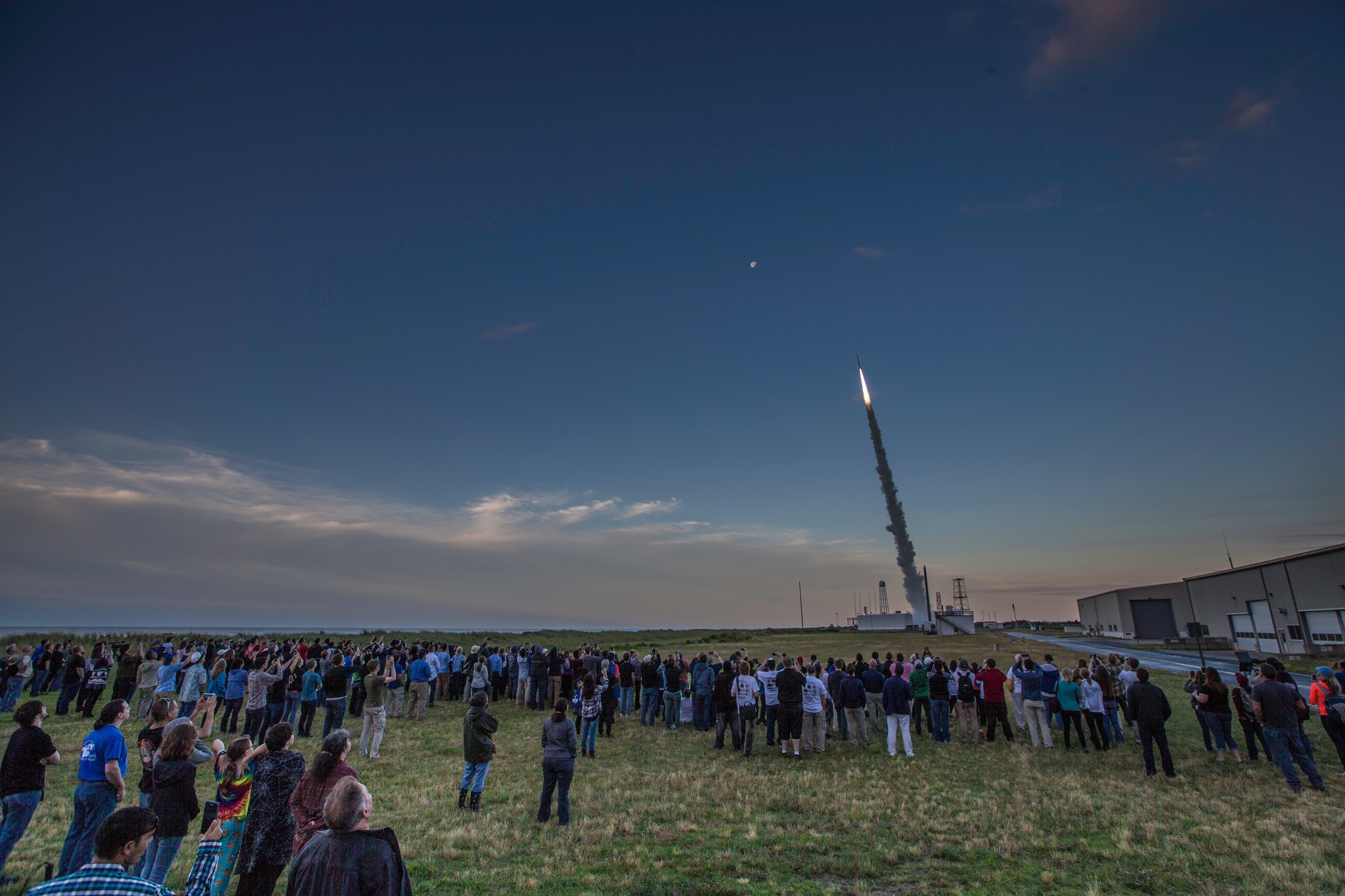 A large group of students watches as a sounding rocket launches in the background.