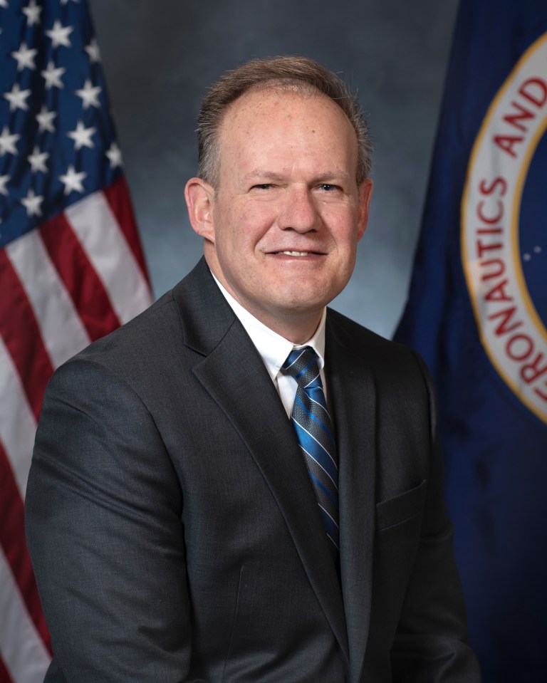 Portrait of Gus Konstantions with U.S. and NASA Flags in background.