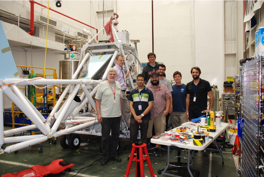 A group of people stands in front of a large metal structure that is the BETTII payload.