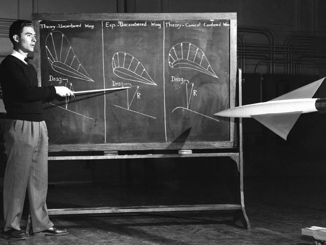 Black and white photo of John W. “Jack” Boyd standing in front of a chalkboard showing diagrams of three different wing shapes.