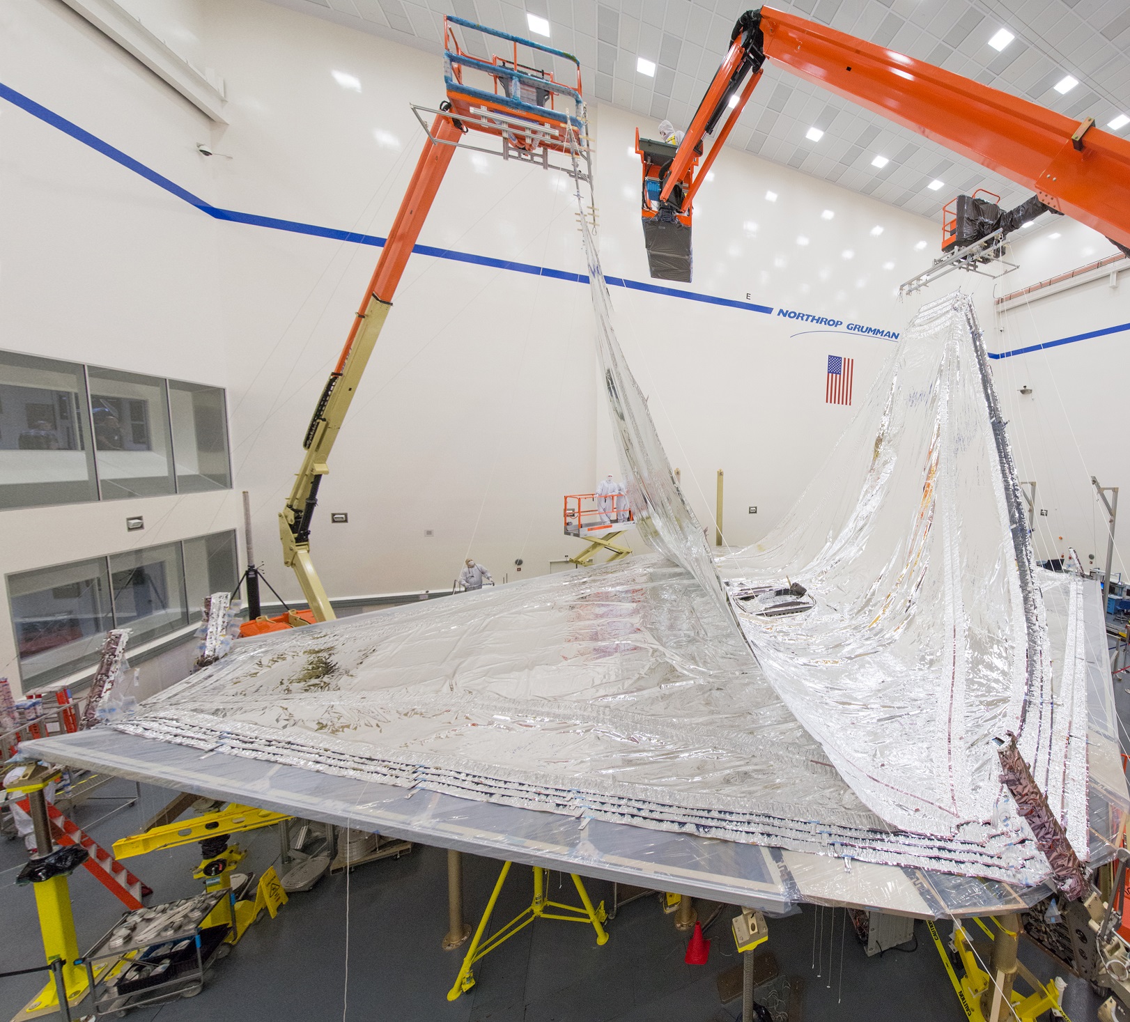 A thin silver kapton layer is added to the sunshield by two orange cranes.