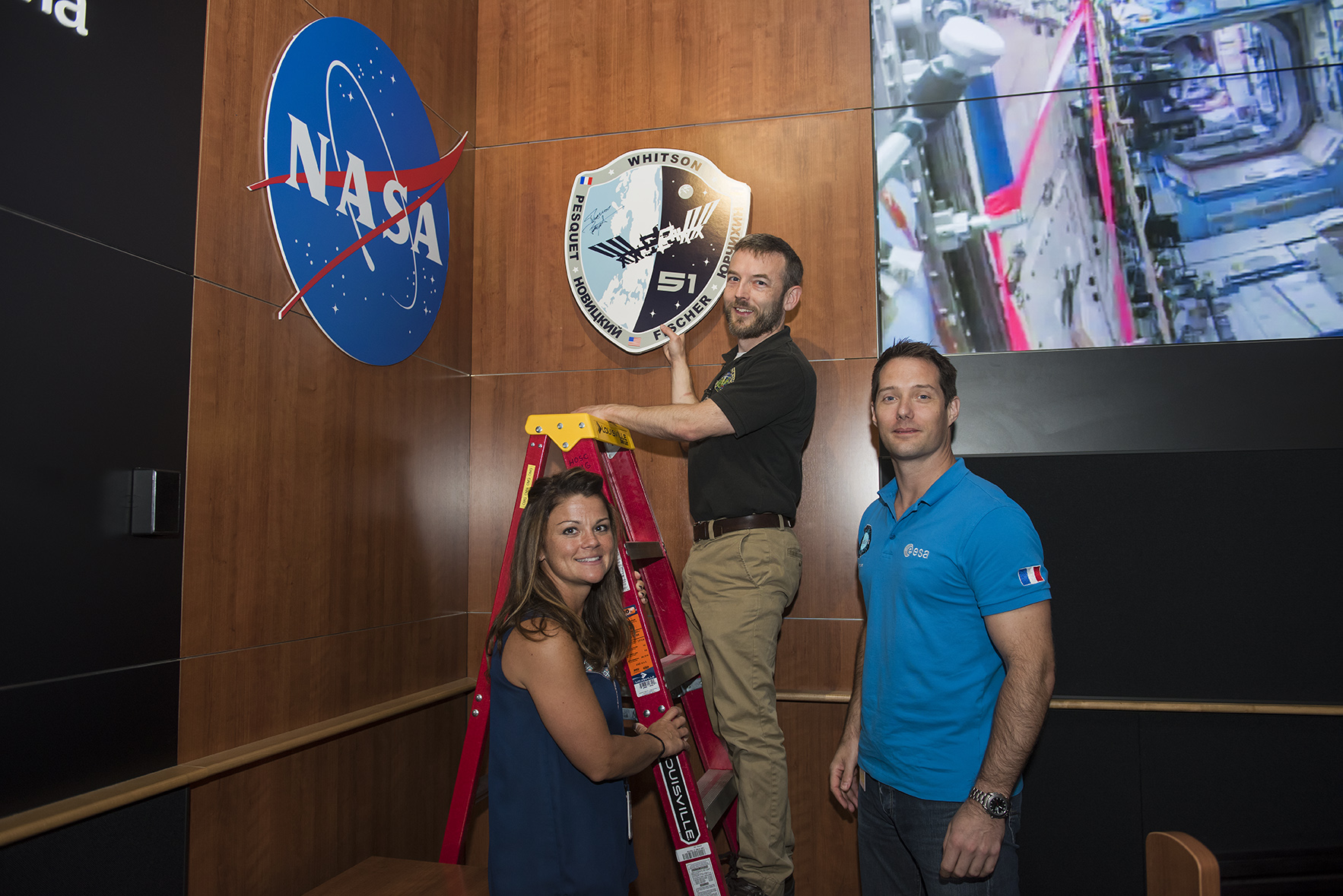 Astronaut Thomas Pesquet, right, helps hang a new mission plaque in the Payload Operations Integration Center control room.