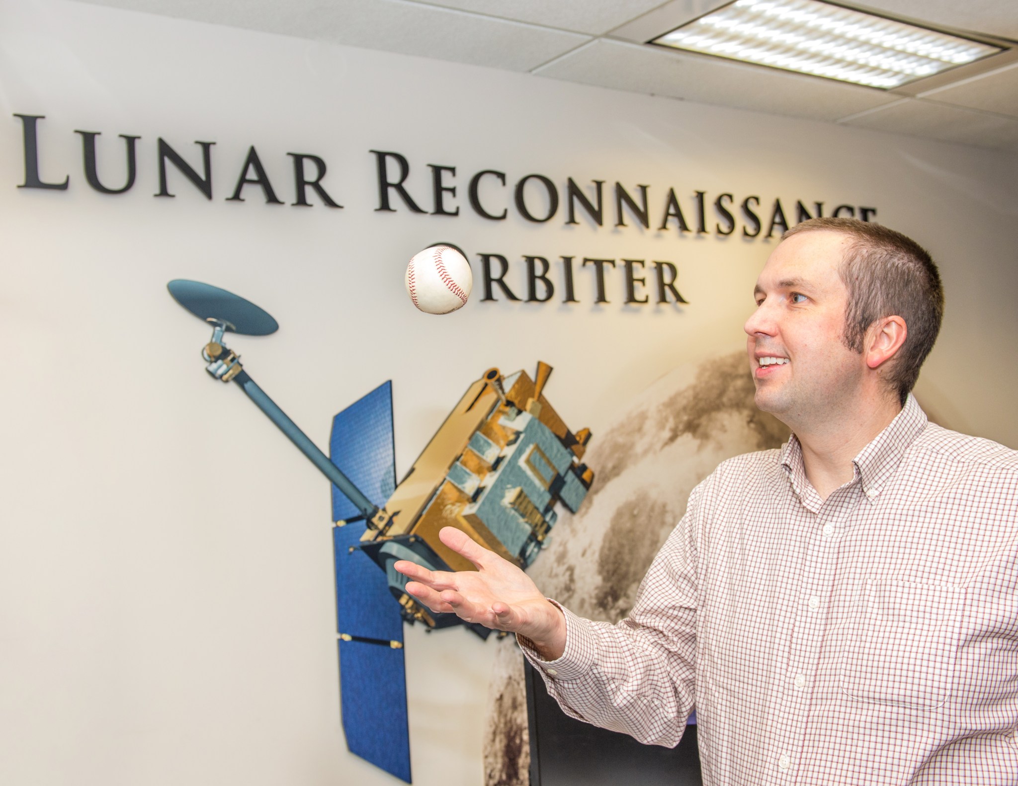Noah Petro tosses a baseball in the air in front of the Lunar Reconnaissance Orbiter model.