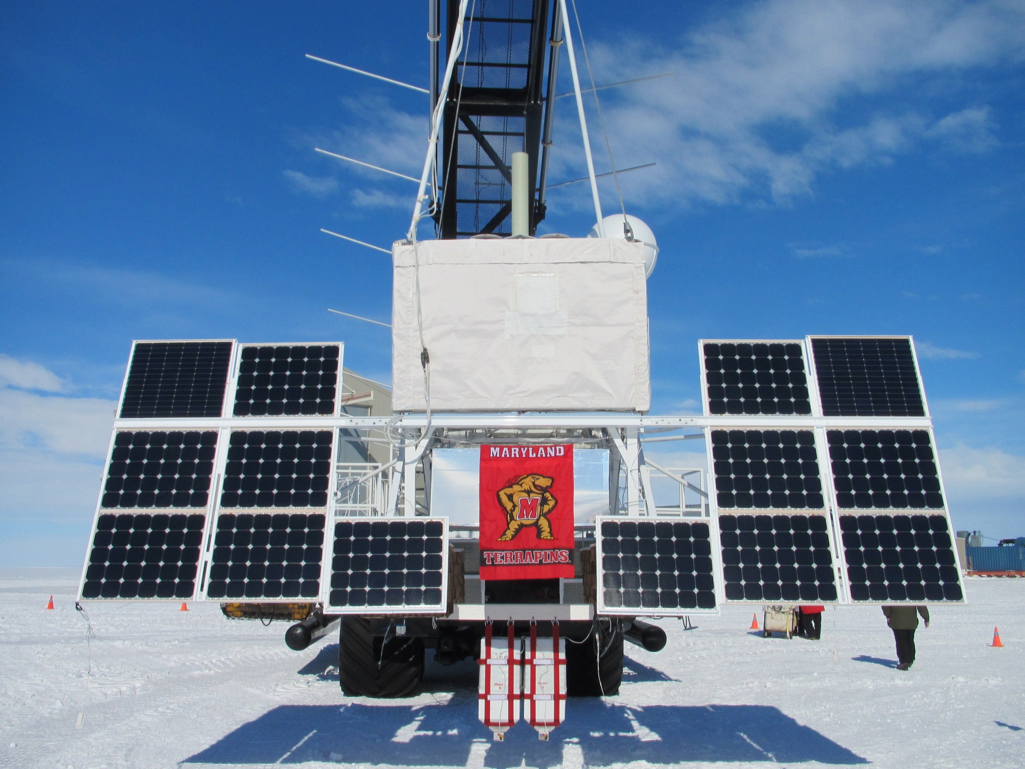 ISS-CREAM, a rectangular white box, hangs from a crane attached to multiple solar panels in a snowy landscape.