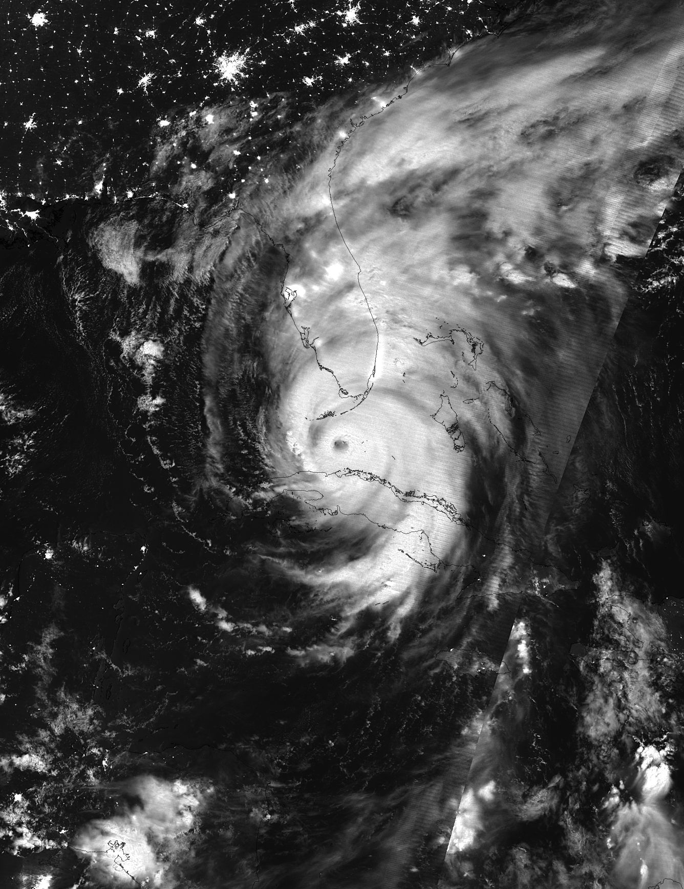 Black and white satellite image of Irma at night, with a clear eye over the ocean and electric lights glowing on land.
