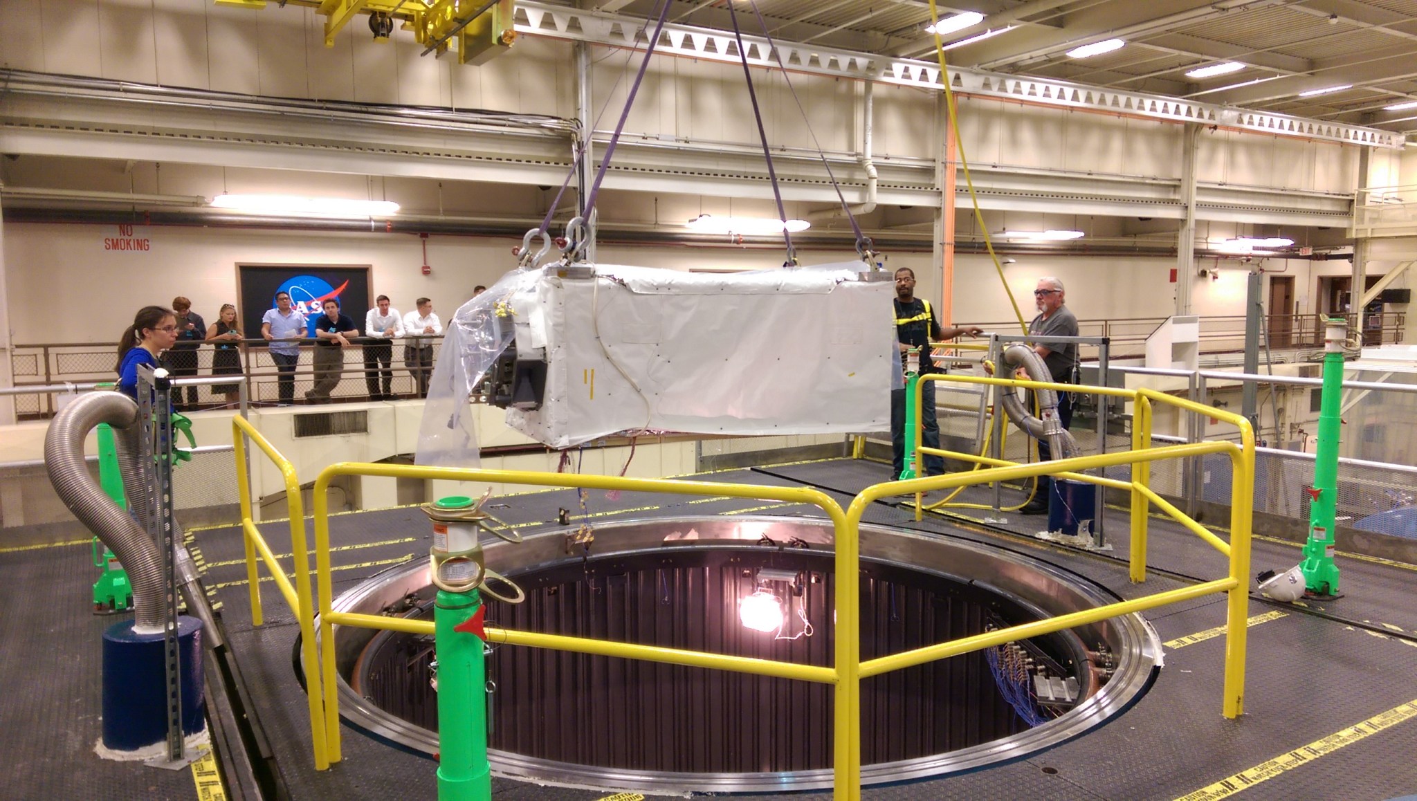 Students stand behind guard rails near a vacuum chamber hole, where the ISS-CREAM experiment is about to be lowered in.