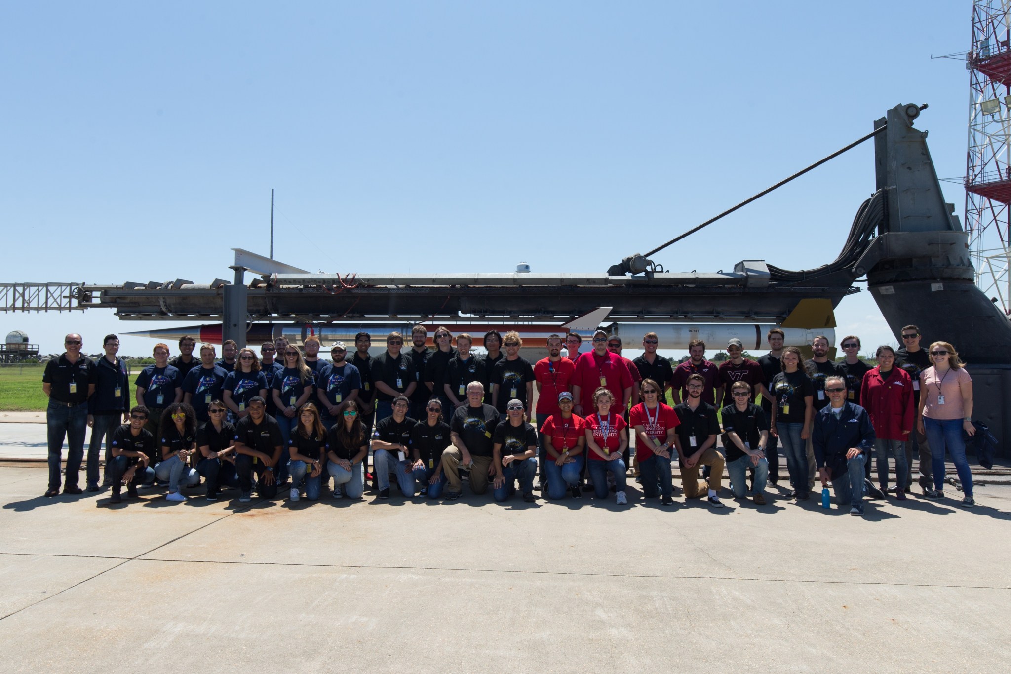 A group of students stands in front of a sounding rocket horizontal on its launch pad.