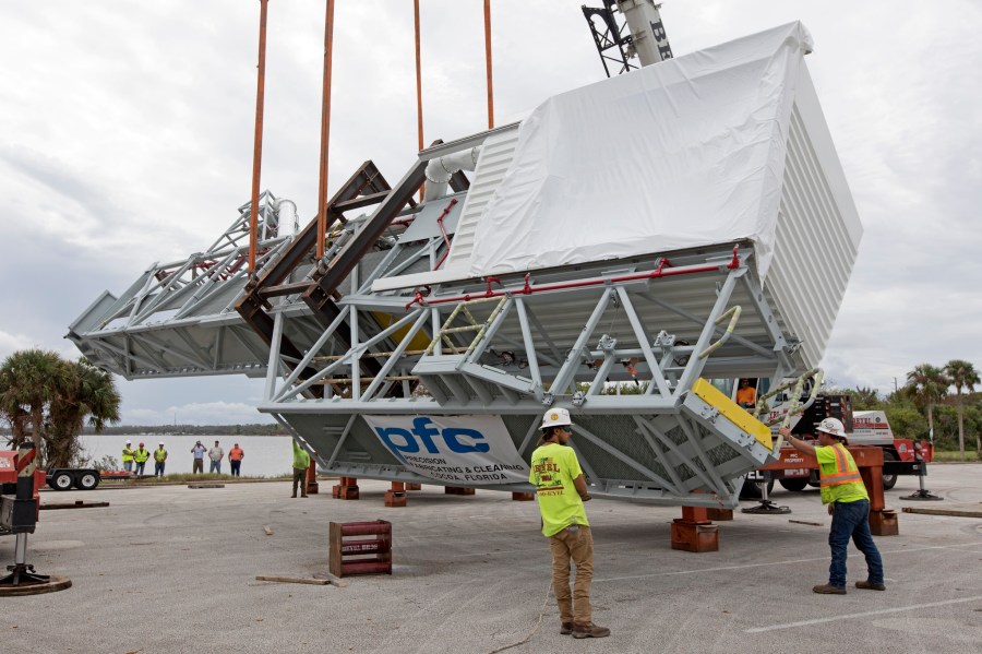 Two heavy-lift cranes are used to tilt and lower the Orion crew access arm onto a work stand in a storage location Oct. 17, 2017, at NASA's Kennedy Space Center in Florida.