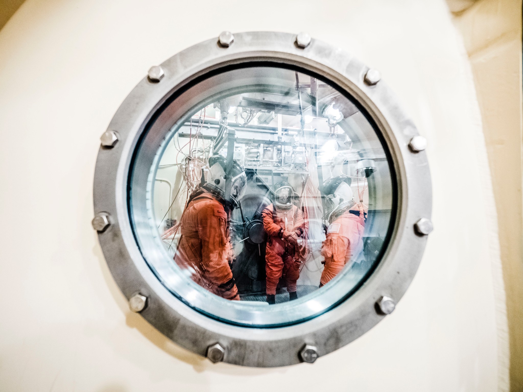 Technicians in pressure suits viewed through round window