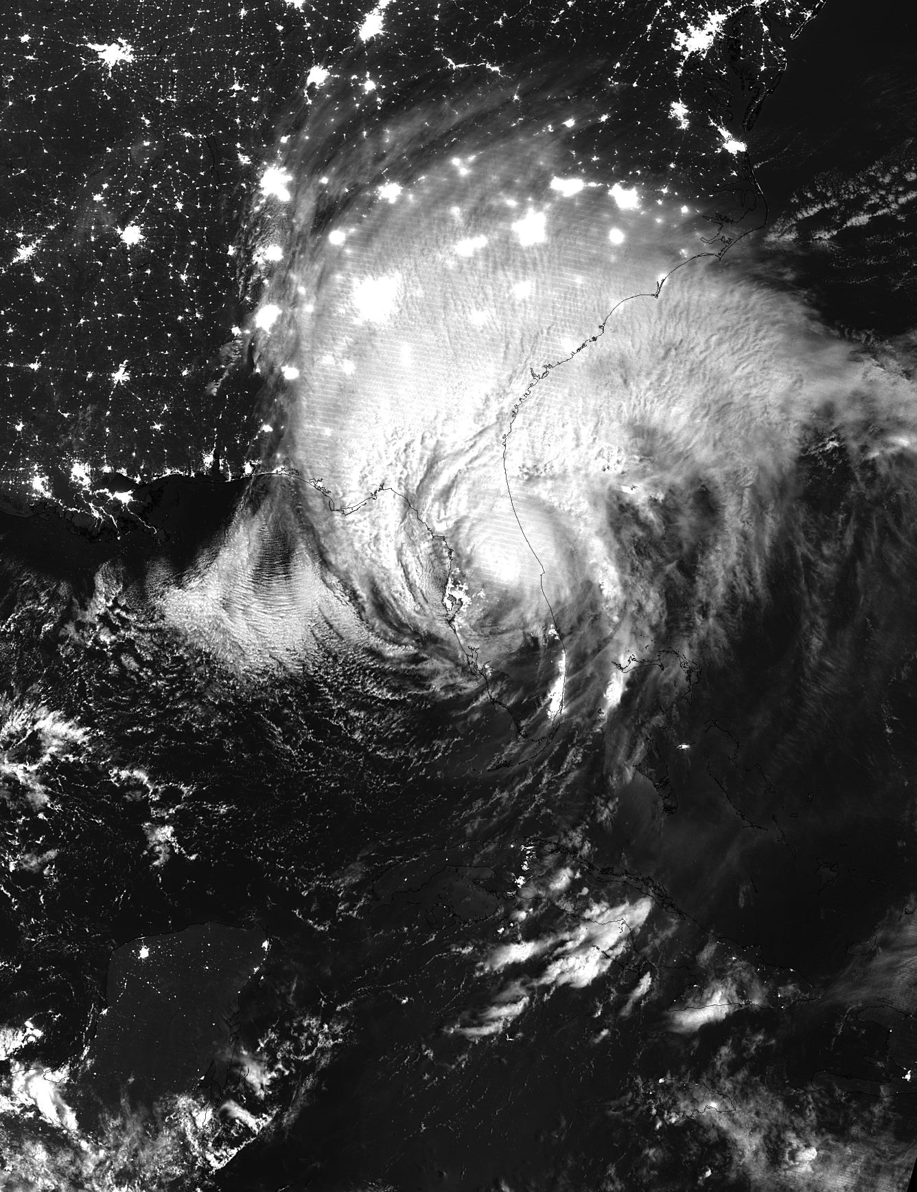 Satellite image of Irma at night, in black and white. Electric lights shine on land under the white cloud over the southeastern US coast.