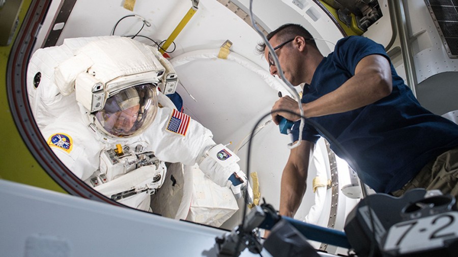 Astronaut in spacesuit inside airlock assisted by another astronaut
