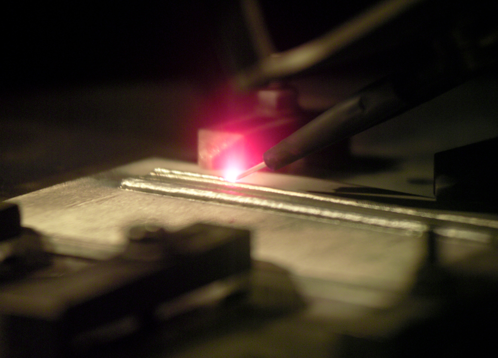 A pen-like tool emits a bright pinkish-red light as part of a 3D printer seen in action.