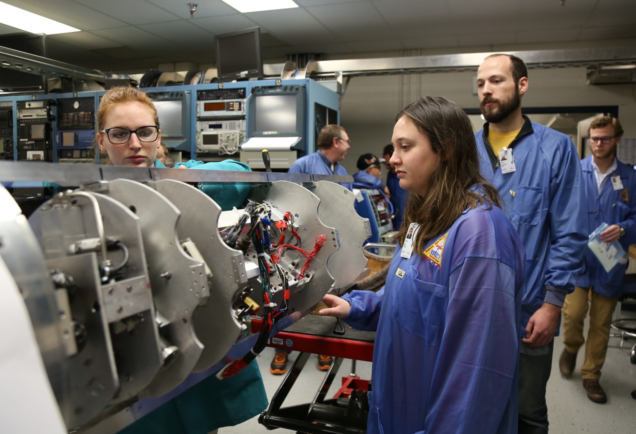 Students in blue anti-static jackets peer into a the payload section of their sounding rocket experiment.