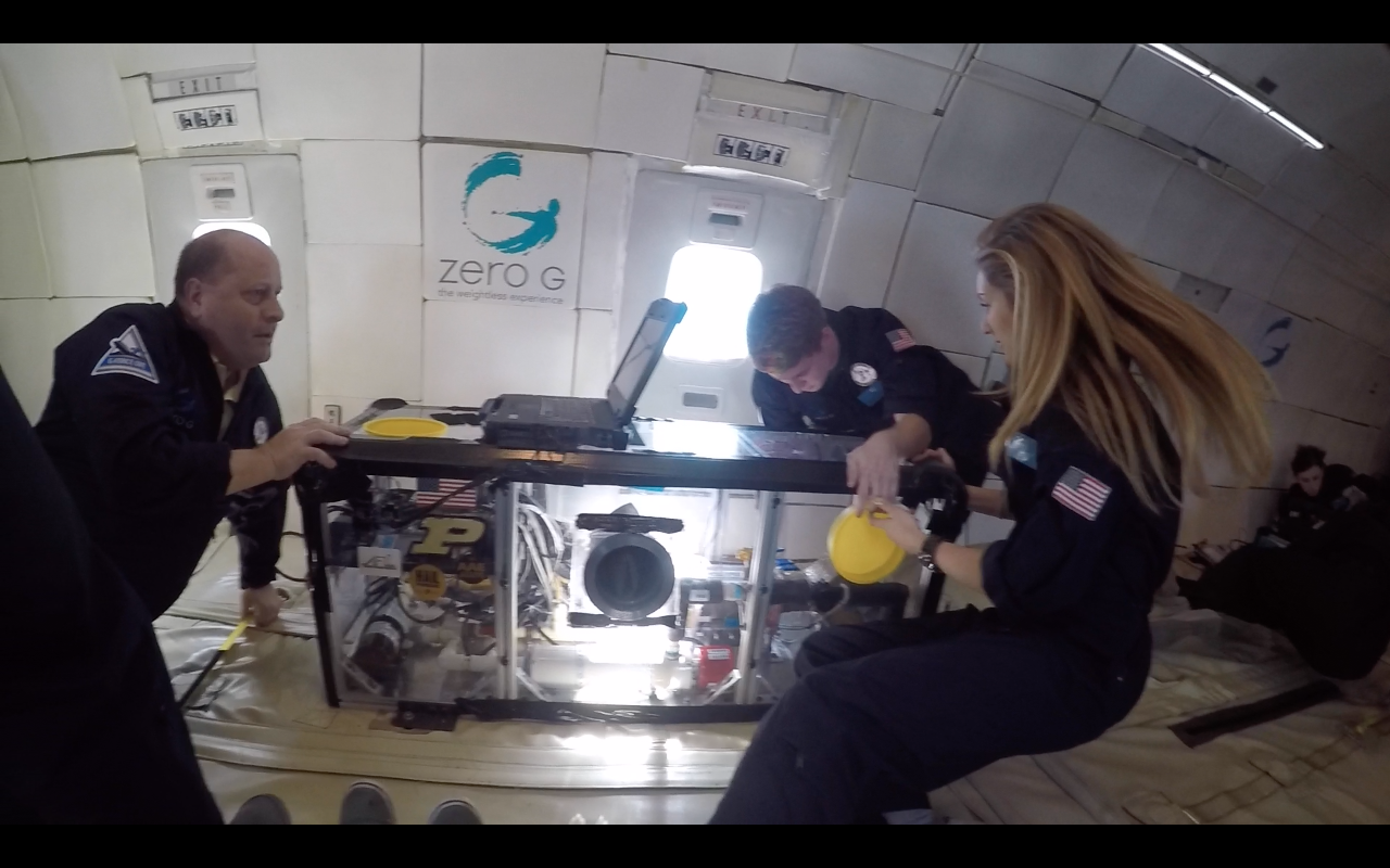 three researchers float in microgravity as they work with their experiment