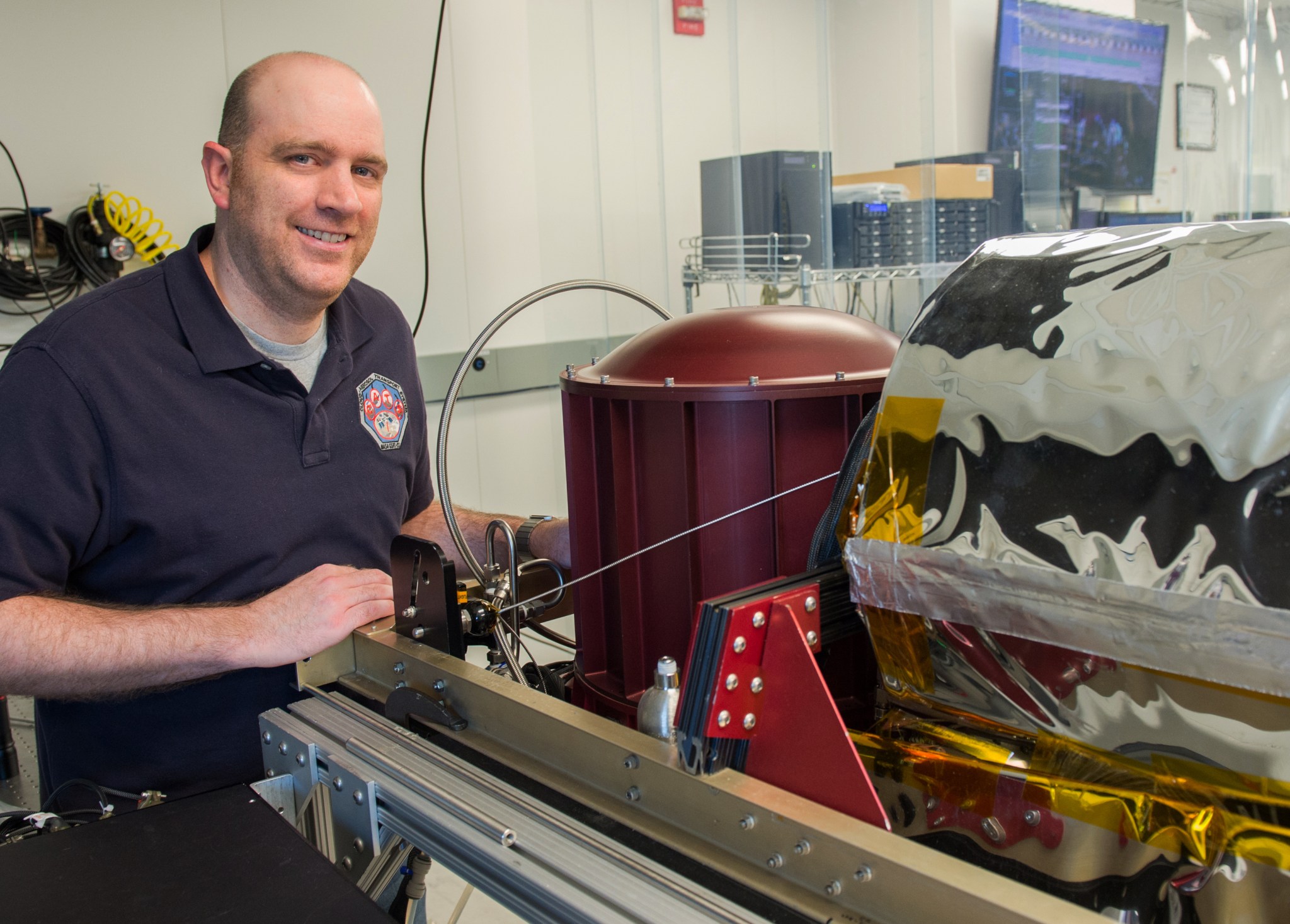 John Yorks, man with fair skin wearing a blue polo stands next to machines in a lab