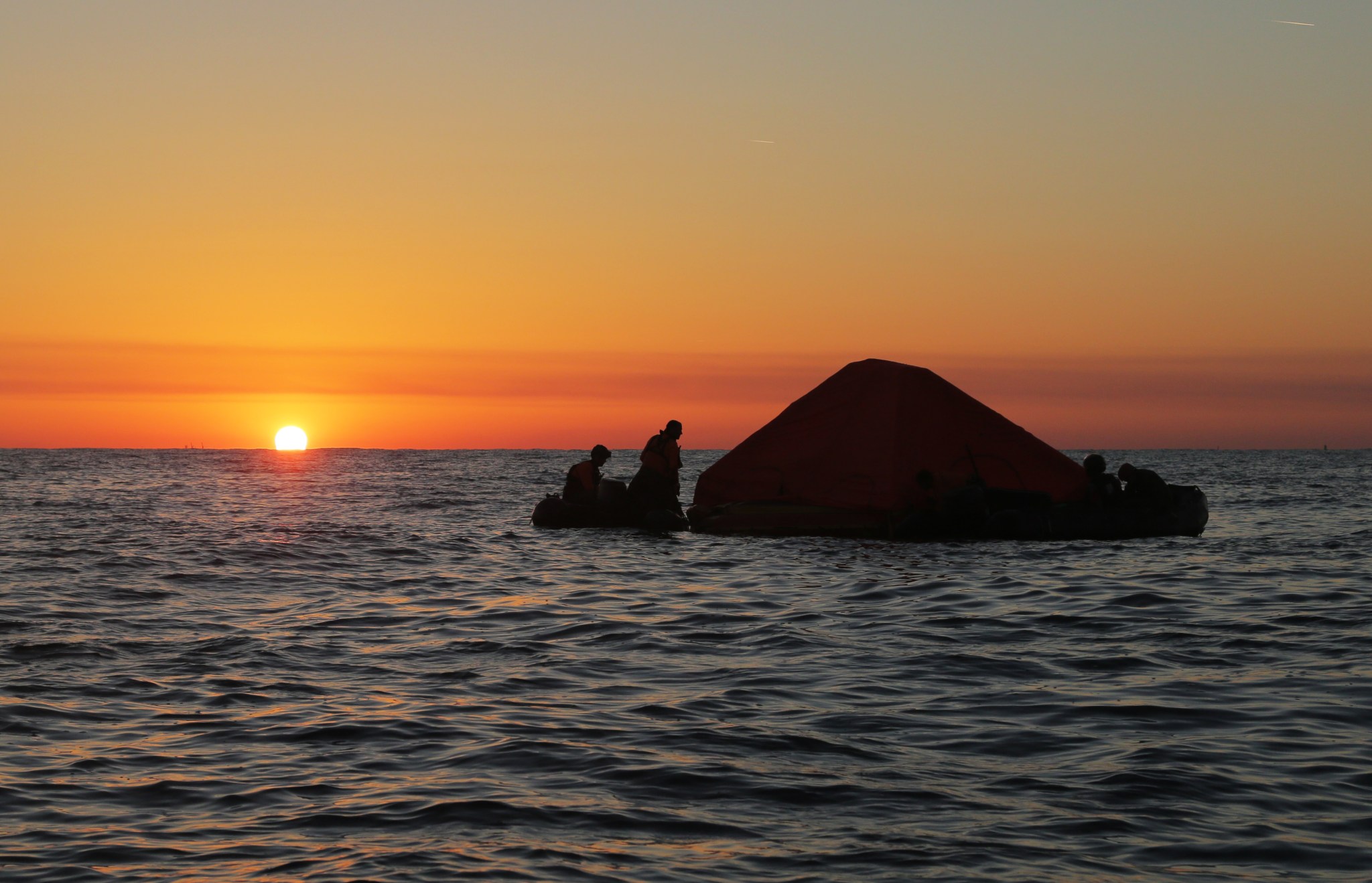 Pararescue specialists secure a covered life raft as the sun sets