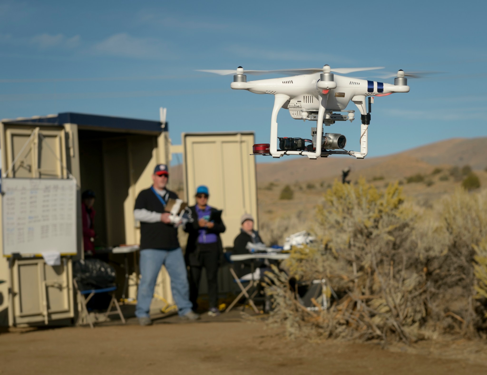 Photograph of drone being flown with operator and observers slightly out-of-focus in the background