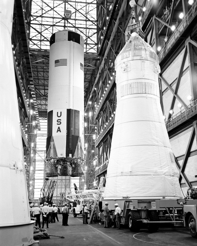 The first stage of the Apollo 10 Saturn V space vehicle is hoisted above the transfer aisle in preparation for erection on a mobile launcher within High Bay 2 of the Vehicle Assembly Building.